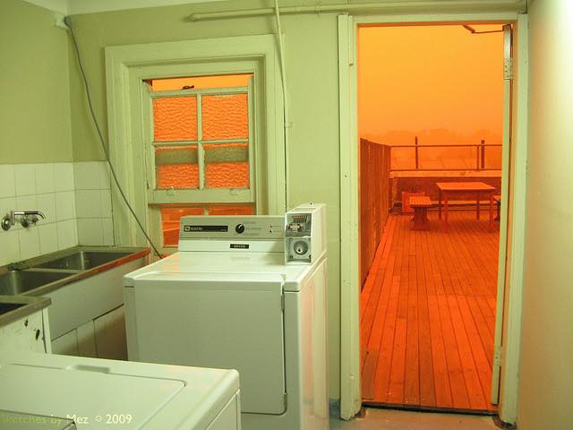 This meme is a photo of a laundry room with a washing machine and dryer. The image is edited to have a bright, sunny yellow color, but the text "I can smell the desperation" is written in a darker, more muted color, implying that the person is feeling overwhelmed and desperate. The image is likely a humorous commentary on the challenges of doing laundry.